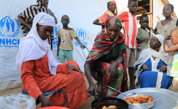 Three young women fry doughnuts in a pan outside a tent