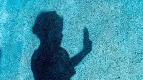 The shadow of a girl holding her hand up against a blue wall
