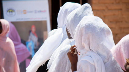 Des femmes portant des voiles blancs sont photographiées de dos alors qu’elles regardent en direction d’une grande affiche représentant une femme et portant le logo de l’UNFPA