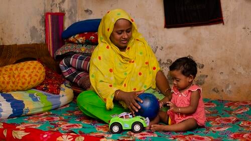 Une mère joue avec son enfant, assise sur un lit.